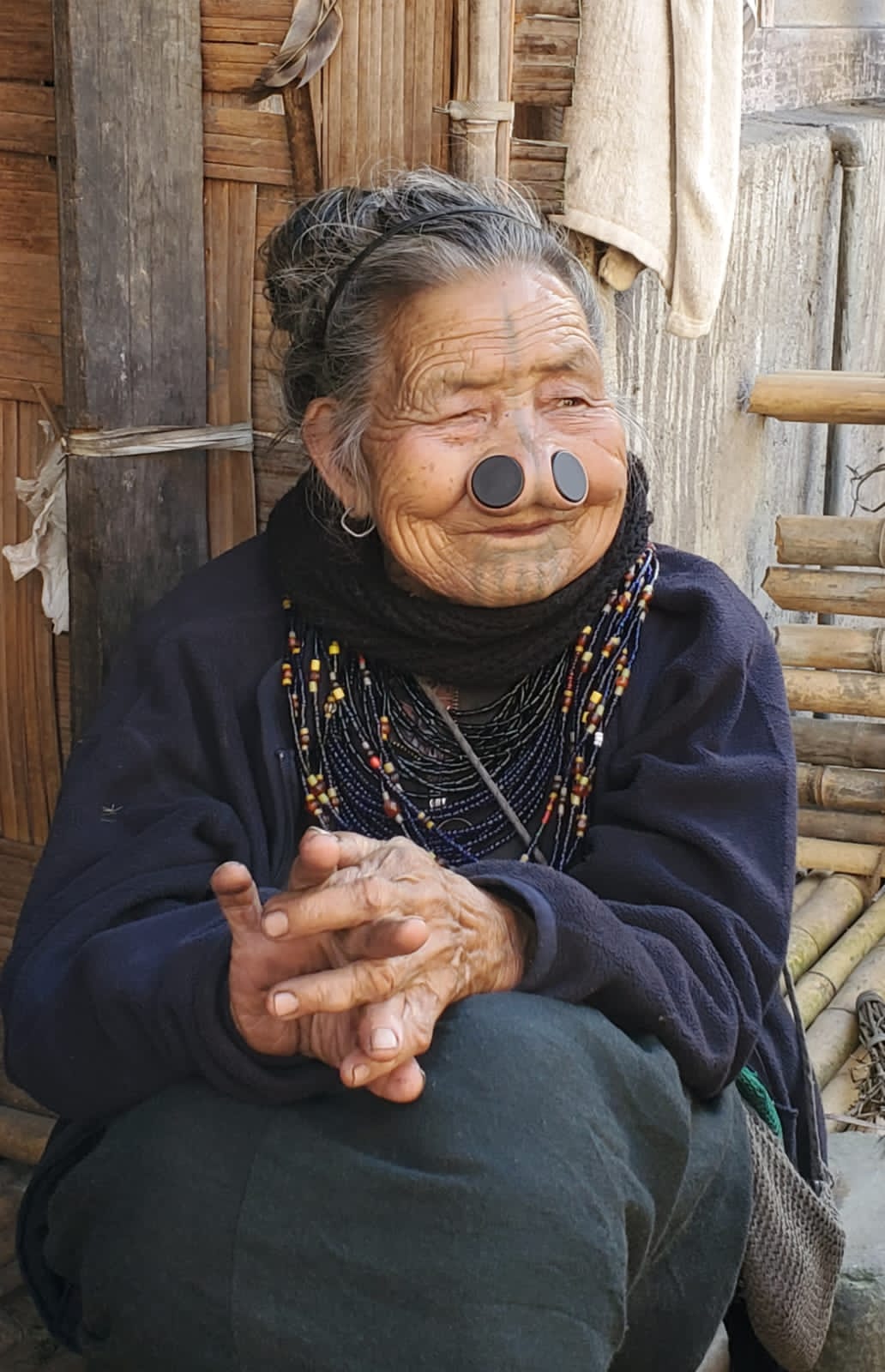 An elderly Apatani woman in Ziro Valley with traditional nose plugs and facial tattoos, wearing a beaded necklace