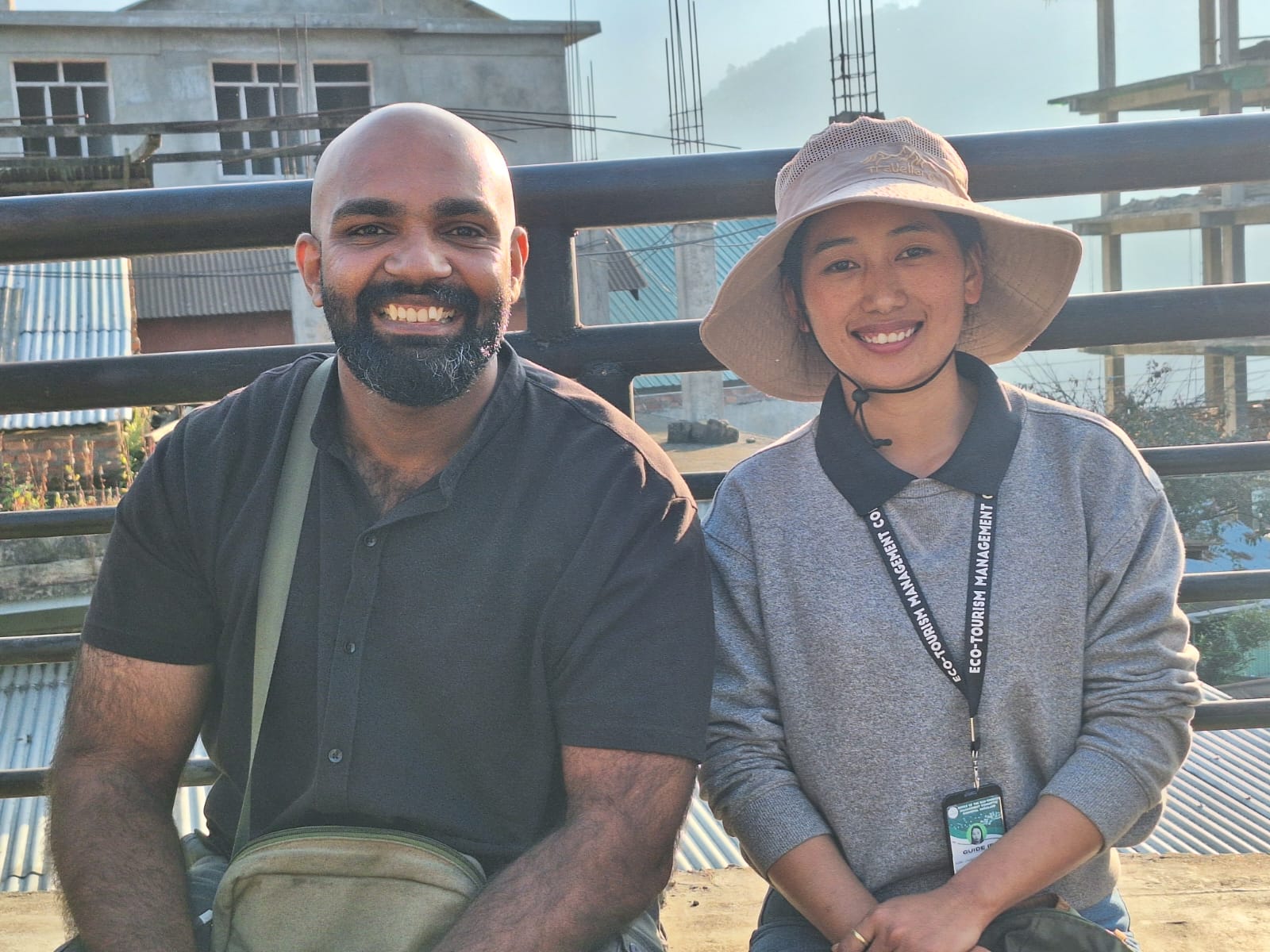 Mahim, the Kerala group leader, seated beside the local Nagaland guide on a bridge railing in the Angami hills, both smiling in the morning sun
