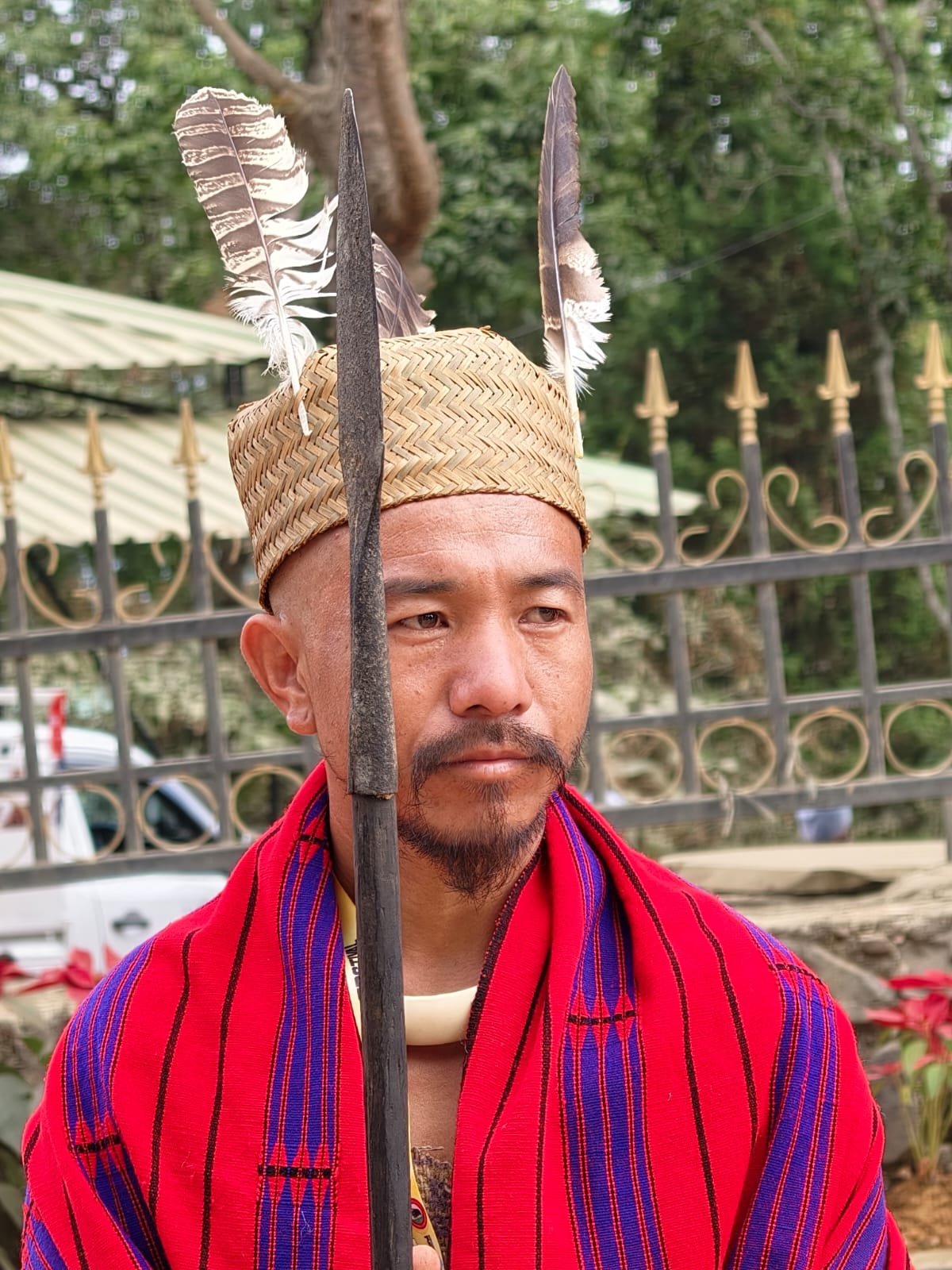 A Naga performer in a bamboo headdress and red-blue striped shawl holding a spear at the Hornbill Festival