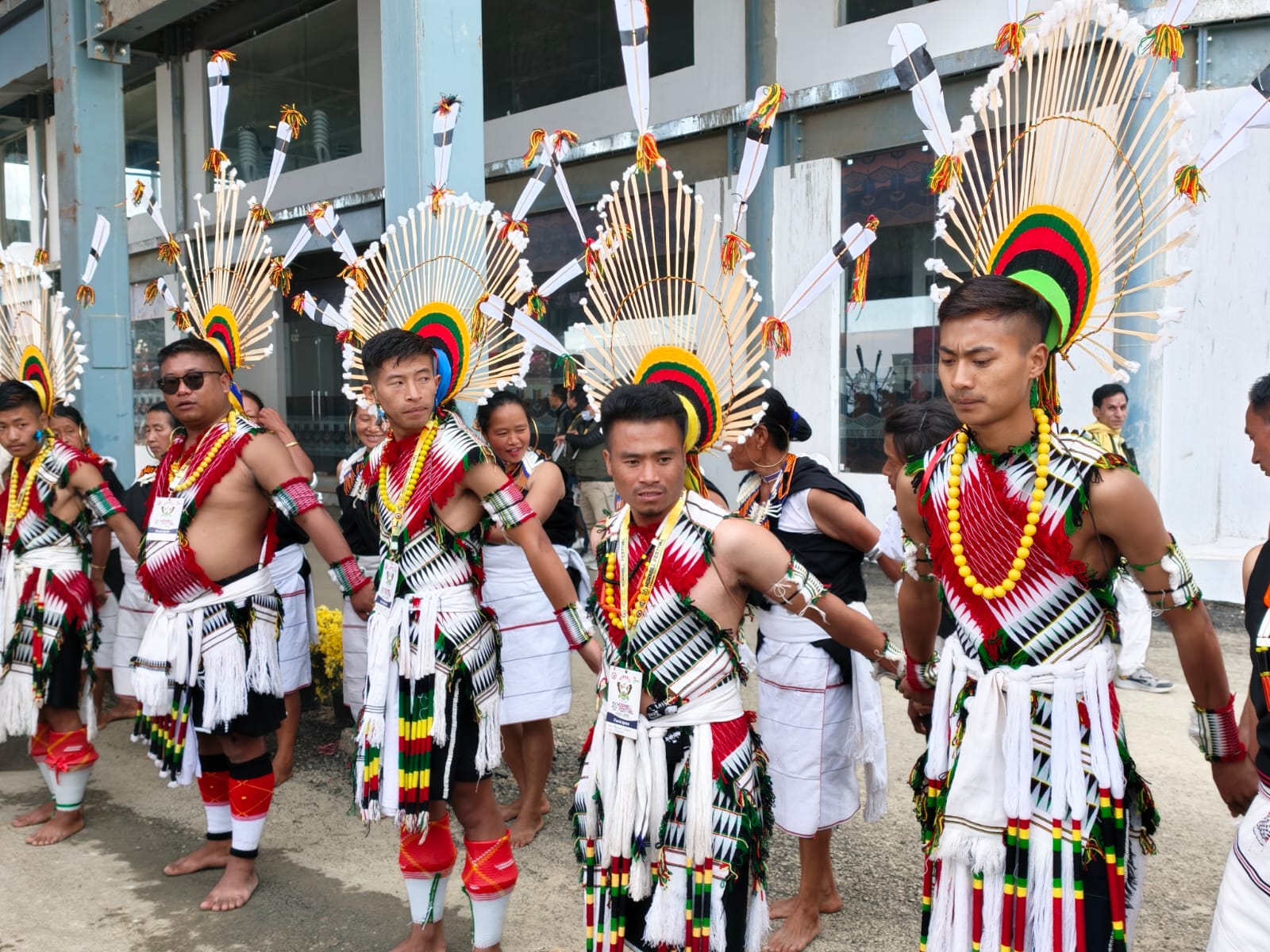 Naga warriors in white and red feathered headdresses preparing for a Hornbill Festival performance