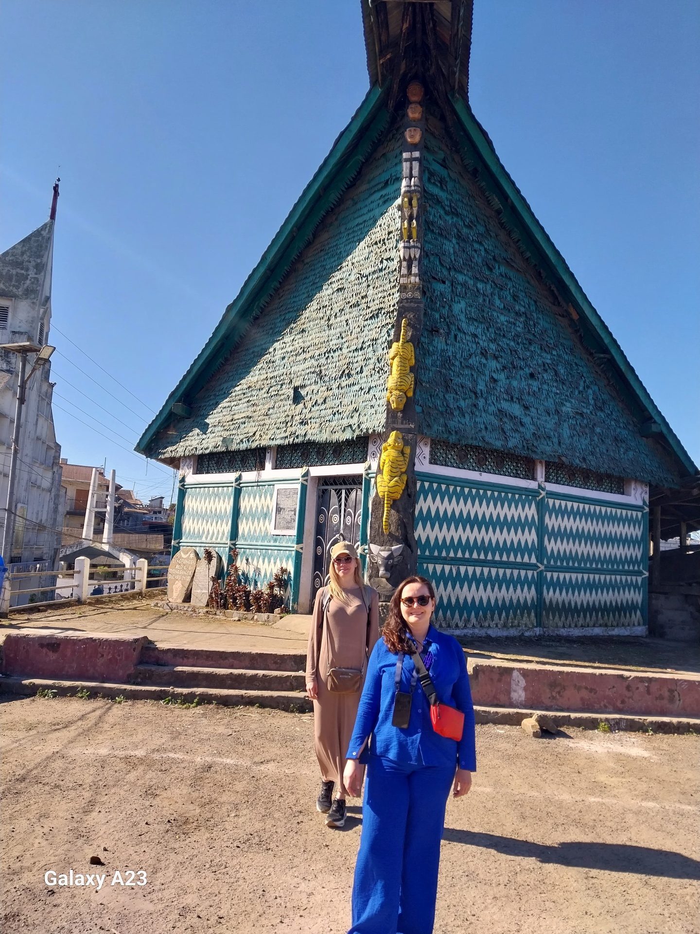 A tall, ornately carved Ao Naga morung with a thatched roof and yellow tiger motifs in Mokokchung